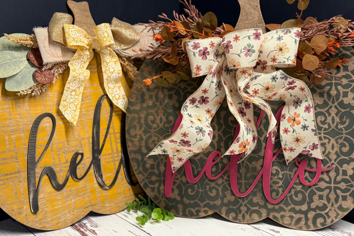 Two hand-painted 18-inch wood pumpkin door hangers with hello lettering and fall bows